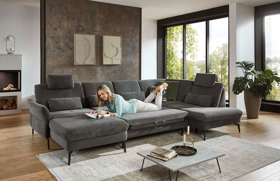 Großes, modernes Ecksofa in Dunkelgrau mit verstellbaren Kopfstützen und Relaxfunktion, stilvoll im Wohnzimmer platziert, ideal für Komfort und Entspannung.